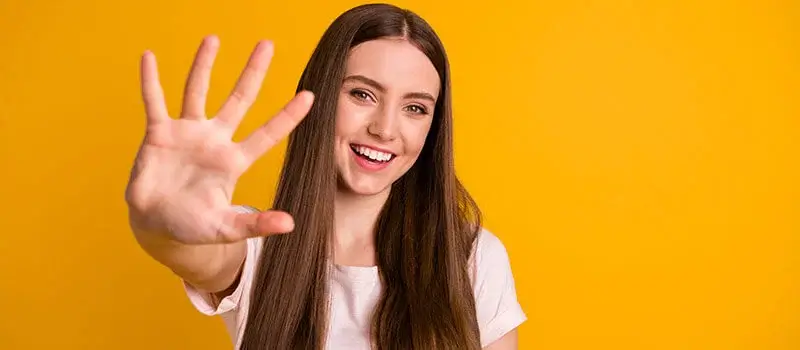 Young woman holding out hard with 5 fingers open wide on Yellow.