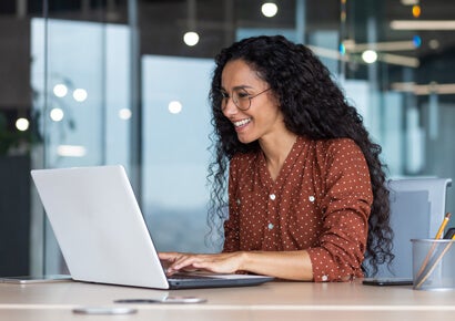 Hispanic woman on laptop in a happy workplace.